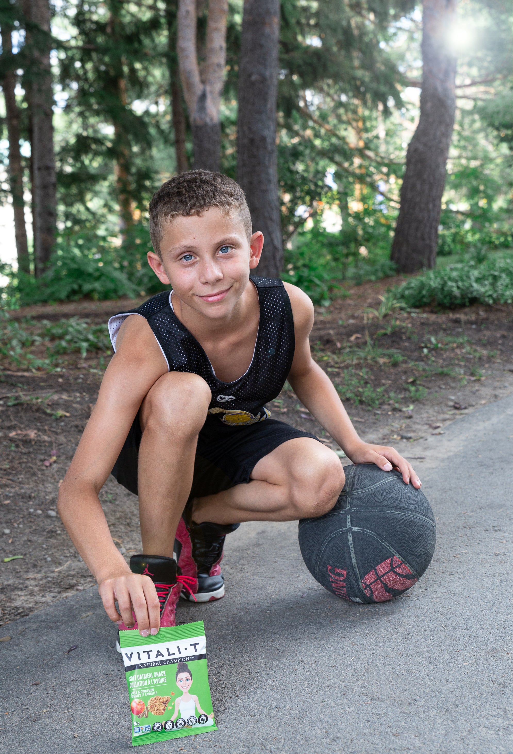 Enfant avec balle de basket ball, qui tient une collation à l'avoine pomme cannelle Vitali-T dans la main. 